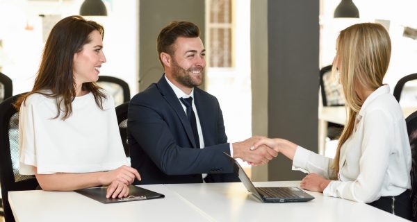 Smiling young couple shaking hands with an insurance agent or investment adviser. Three people meeting in an office reaching an agreement